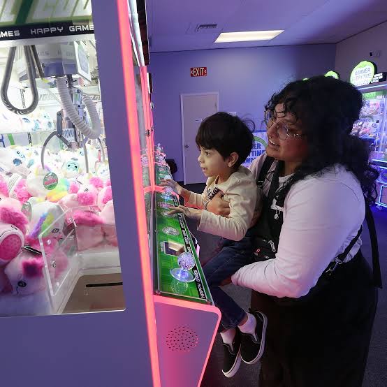 A child and adult playing a claw machine filled with plush